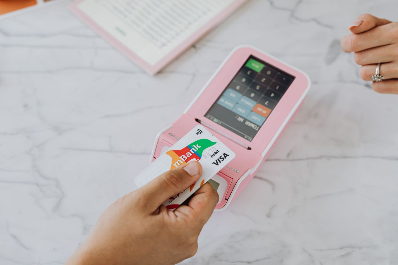 Main tenant une carte sans contact sur un terminal POS rose pour une transaction sans fil.