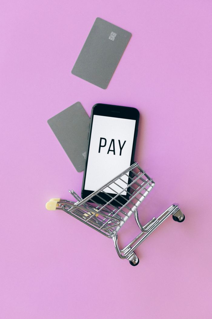 Vue de dessus d’un smartphone dans un caddie avec des cartes de crédit sur fond violet.